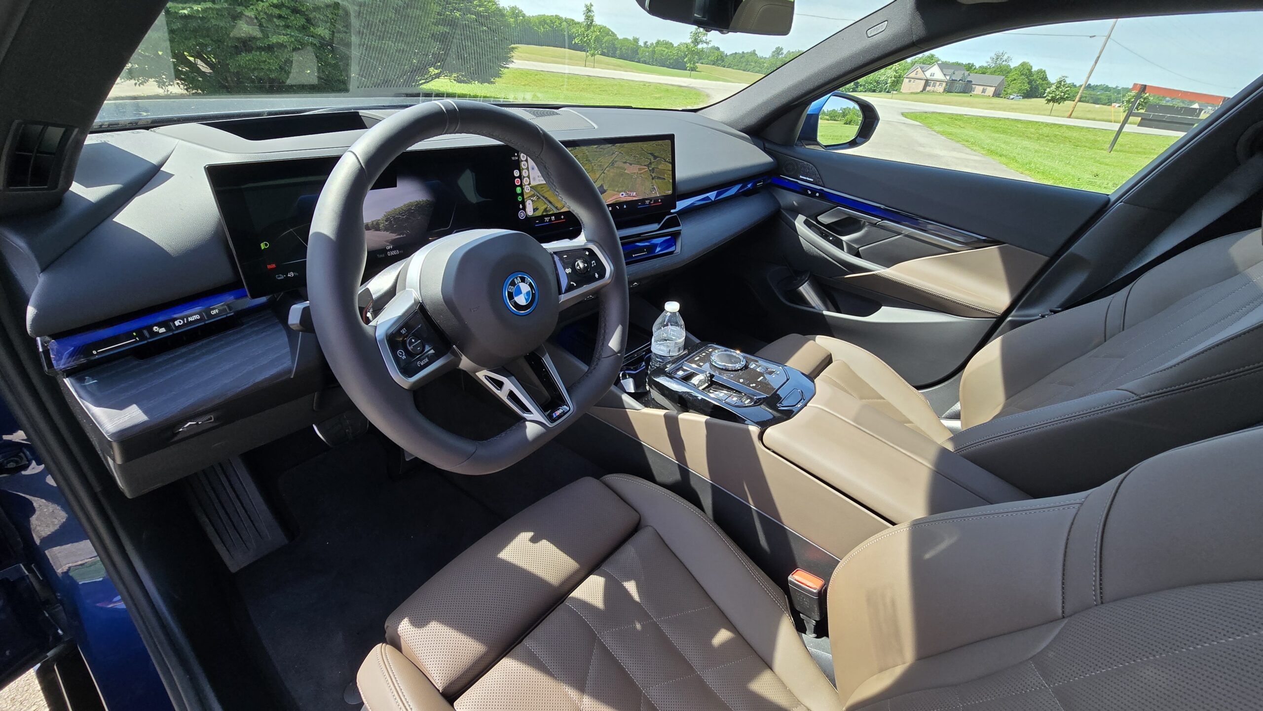 Driver's seat interior view showing the steering wheel, dashboard, and infotainment screen of the 2026 BMW 5-Series